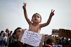A Syrian refugee holds a child carrying a placard which reads \